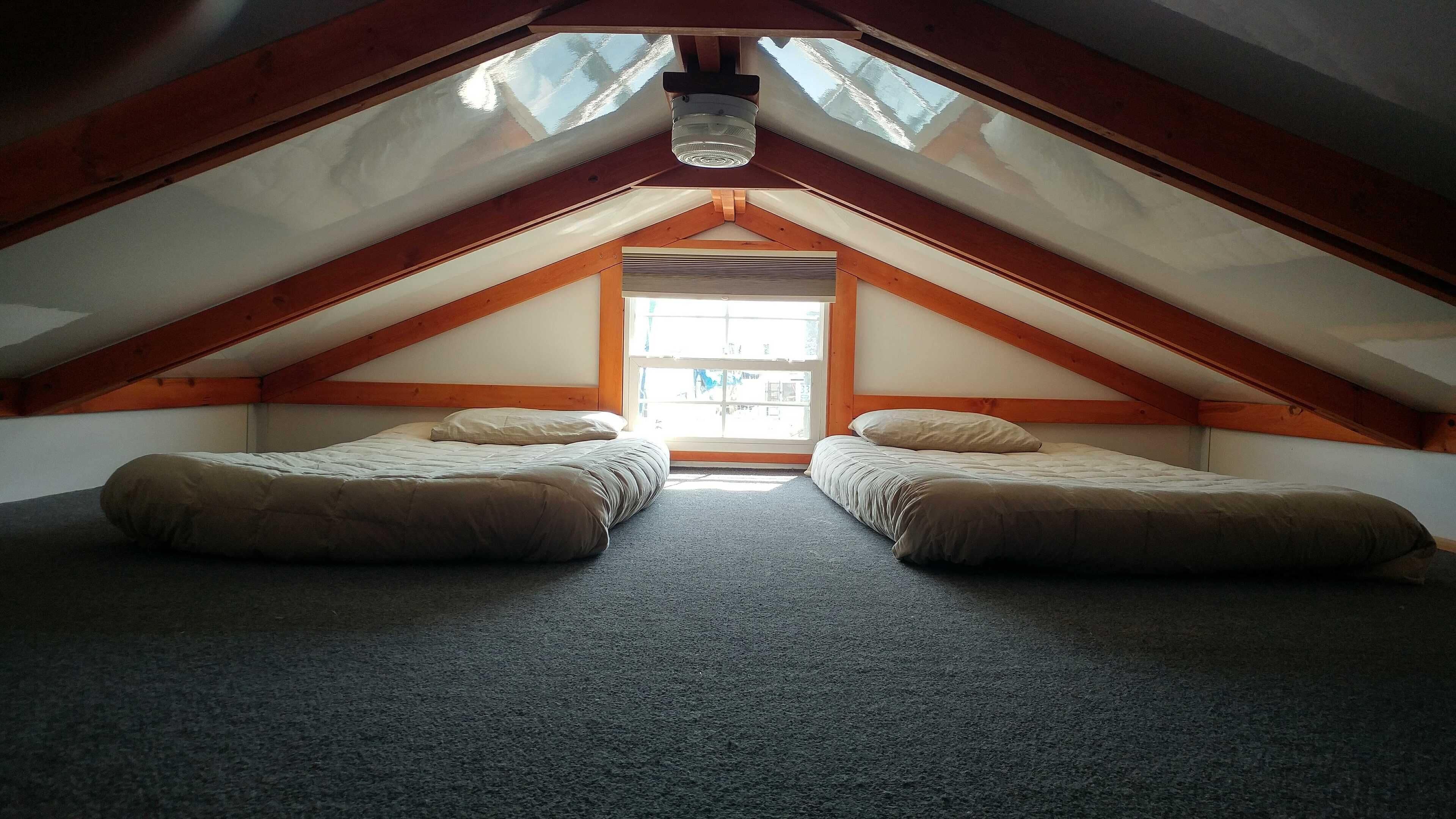 Dormitorio en ático con dos camas, vigas de madera y tragaluces.