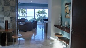 A spacious living area with a view of palm trees and the ocean, a modern kitchen with bar stools, and a dining table. - Paradise Perfected! Your Exclusive Beachfront Escape in Bucerías. (Bucerias)