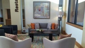 A modern living room with a grey sofa, two armchairs, a coffee table, and a colorful rug. A painting hangs on the wall, and a lamp is on a side table. - 3 BR/3BH, 3 miles to Disney, Gates Resort, Pool with Water Slides (Kissimmee)