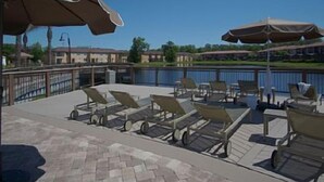 A poolside area with lounge chairs and umbrellas, a clear view of the pool, and a building in the background. - 3 BR/3BH, 3 miles to Disney, Gates Resort, Pool with Water Slides (Kissimmee)