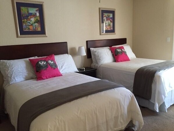 Two beds with white linens, pink owl pillows, and dark headboards.