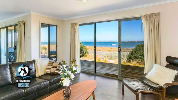 A spacious living room with a large sliding glass door leading to a balcony with a view of the sea. - Absolute Waterfront Views + Kayaks (Noonameena)