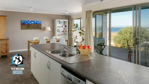 A modern kitchen with a large island, a dishwasher, and a view of the outdoors. - Absolute Waterfront Views + Kayaks (Noonameena)
