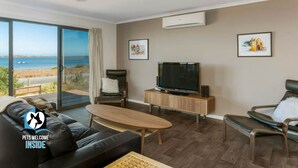 A modern living room with a large TV, comfortable seating, and a view of the sea. - Absolute Waterfront Views + Kayaks (Noonameena)