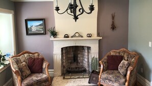 A room with a fireplace, two upholstered chairs, a chandelier, and a framed picture on the wall. - Manti Cottage, Historic Pioneer Home (Manti)