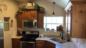 A kitchen with wooden cabinets, stainless steel appliances, a granite countertop, and a window with a view. - Manti Cottage, Historic Pioneer Home (Manti)