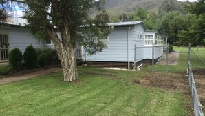 A residential property with a well-maintained lawn, a large tree, and a house with a grey exterior.