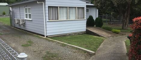 Una casa móvil de un piso con un pequeño patio delantero, un camino de grava y un área cercada.