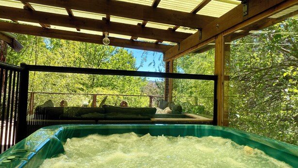 Ein Whirlpool unter einer Holzhütte mit Blick auf einen üppigen, grünen Wald.