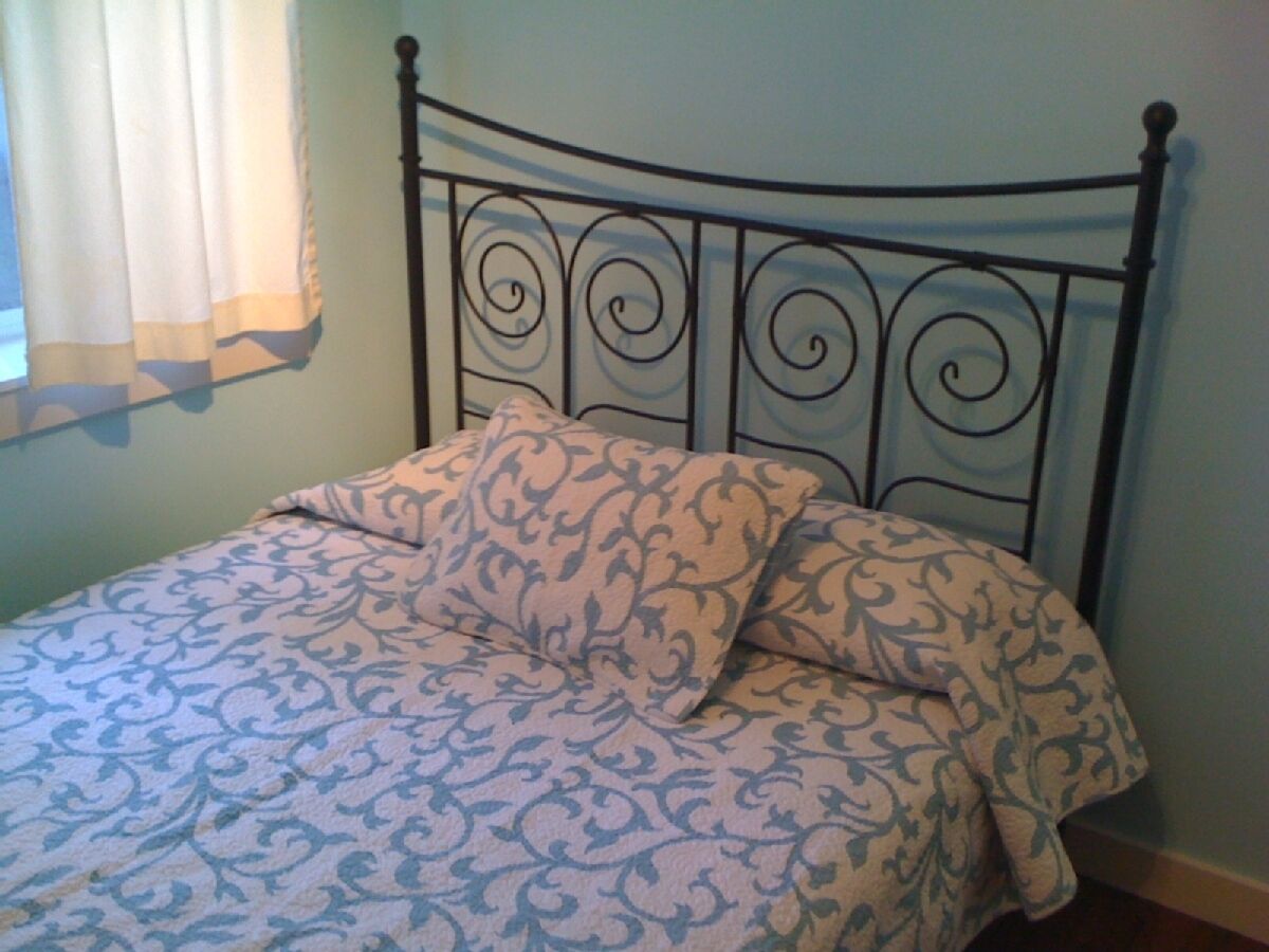 Un lit avec une couvre-lit à motifs et des oreillers, une tête de lit en métal et une fenêtre avec des rideaux.