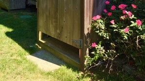 A wooden shed with a hinged door, located in a backyard with a wooden fence, a yellow umbrella, and pink flowers.
