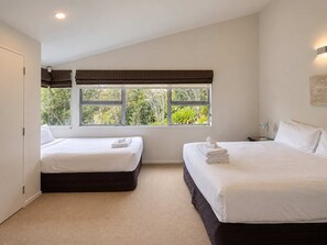 A bedroom with two beds, a window with a view of greenery, and a ceiling light.