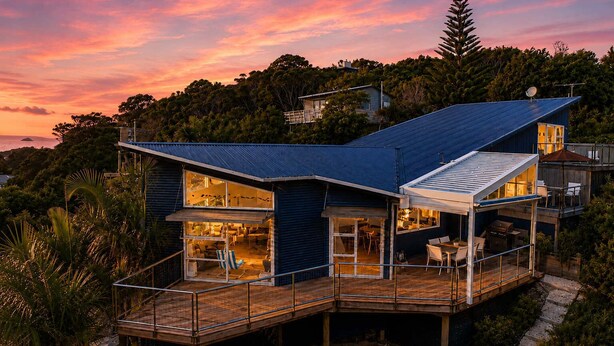 A modern house with a deck, large windows, and a satellite dish. - The Palms - Sea Views near Sandy Bay (Sandy Bay (Waiheke))
