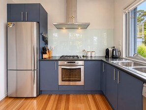 A modern kitchen with a stainless steel refrigerator, gas stove, oven, and a large window providing a view of greenery outside. - The Palms - Sea Views near Sandy Bay (Sandy Bay (Waiheke))