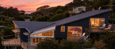 Une maison moderne dotée d’une grande terrasse, d’une véranda en verre et offrant une vue sur le coucher de soleil.