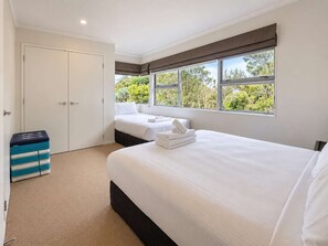 Une chambre d’hôtel avec un grand lit, un lit plus petit, une armoire et une fenêtre donnant sur un paysage verdoyant.