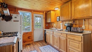 A wooden cabin kitchen with a stove, sink, cabinets, and a coffee maker. - Rangeley Manor 2 | Great Cabin with Shared Access to Rangeley Lake. (Rangeley)