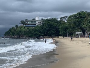 A beach with waves, people, and a building on a hill.