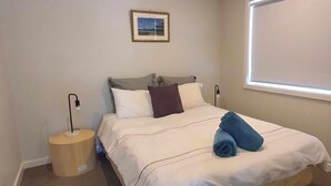 A neatly made bed with white bedding and a blue towel, a bedside lamp, and a framed picture on the wall. - Central Sojourn on Wilcox Unit 1 - Central two bedroom apartment with a queen and double bed (Albury)