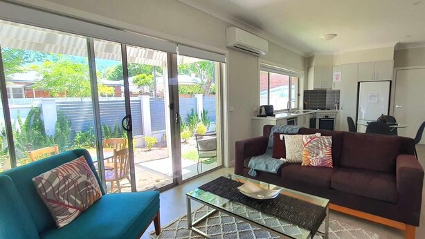 A living room with a sofa, a coffee table, and a sliding glass door leading to a patio. - Central Sojourn on Wilcox Unit 1 - Central two bedroom apartment with a queen and double bed (Albury)