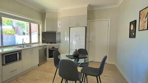 A modern kitchen with a dining area, large windows, and a view of the outside. - Central Sojourn on Wilcox Unit 1 - Central two bedroom apartment with a queen and double bed (Albury)