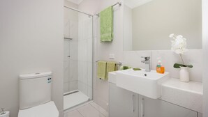 A modern bathroom with a toilet, shower, sink, and mirror. - Central Sojourn on Wilcox Unit 1 - Central two bedroom apartment with a queen and double bed (Albury)