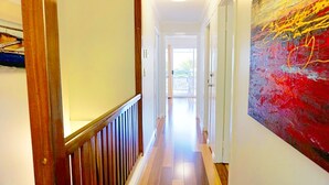 Un pasillo con barandillas de madera, un cuadro abstracto grande en la pared derecha y una puerta que da a un balcón.