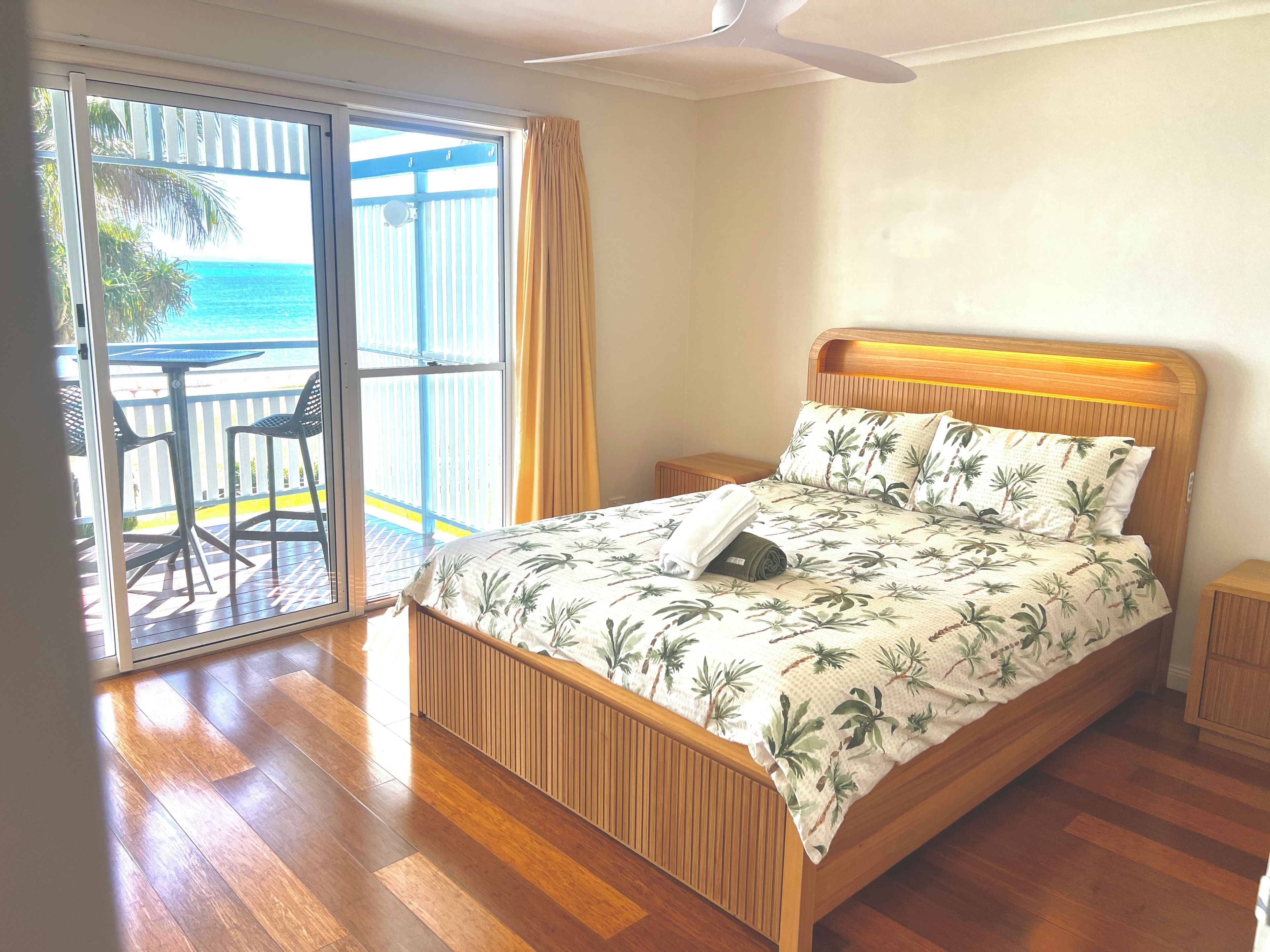 Een slaapkamer met een houten bed, een plafondventilator en uitzicht op de oceaan door een schuifdeur.