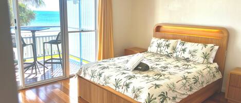 Een slaapkamer met een houten bed, een plafondventilator en uitzicht op de oceaan door een schuifdeur.