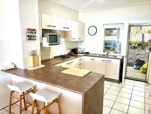 A kitchen with a central island, bar stools, a microwave, a toaster, and a clock on the wall. - Villa 15 Tangalooma Resort Moreton Island (Moreton Island)
