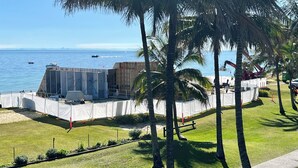 Una obra en construcción con una gran estructura metálica, palmeras y una vista despejada del océano.