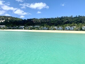 A beach resort with clear turquoise water, a sandy shore, and a backdrop of lush green hills. - Villa 15 Tangalooma Resort Moreton Island (Moreton Island)