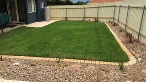 A backyard with a well-maintained lawn, a patio area, and a variety of plants and rocks.