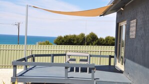 A balcony with a view of the sea, a wooden deck, and a building with a window.