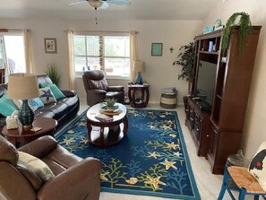A living room with a sofa, armchairs, a coffee table, a TV stand, and a blue rug with a leaf pattern.
