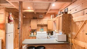 Cocina rústica de cabaña de madera con una isla central, dos taburetes de bar y armarios de madera.