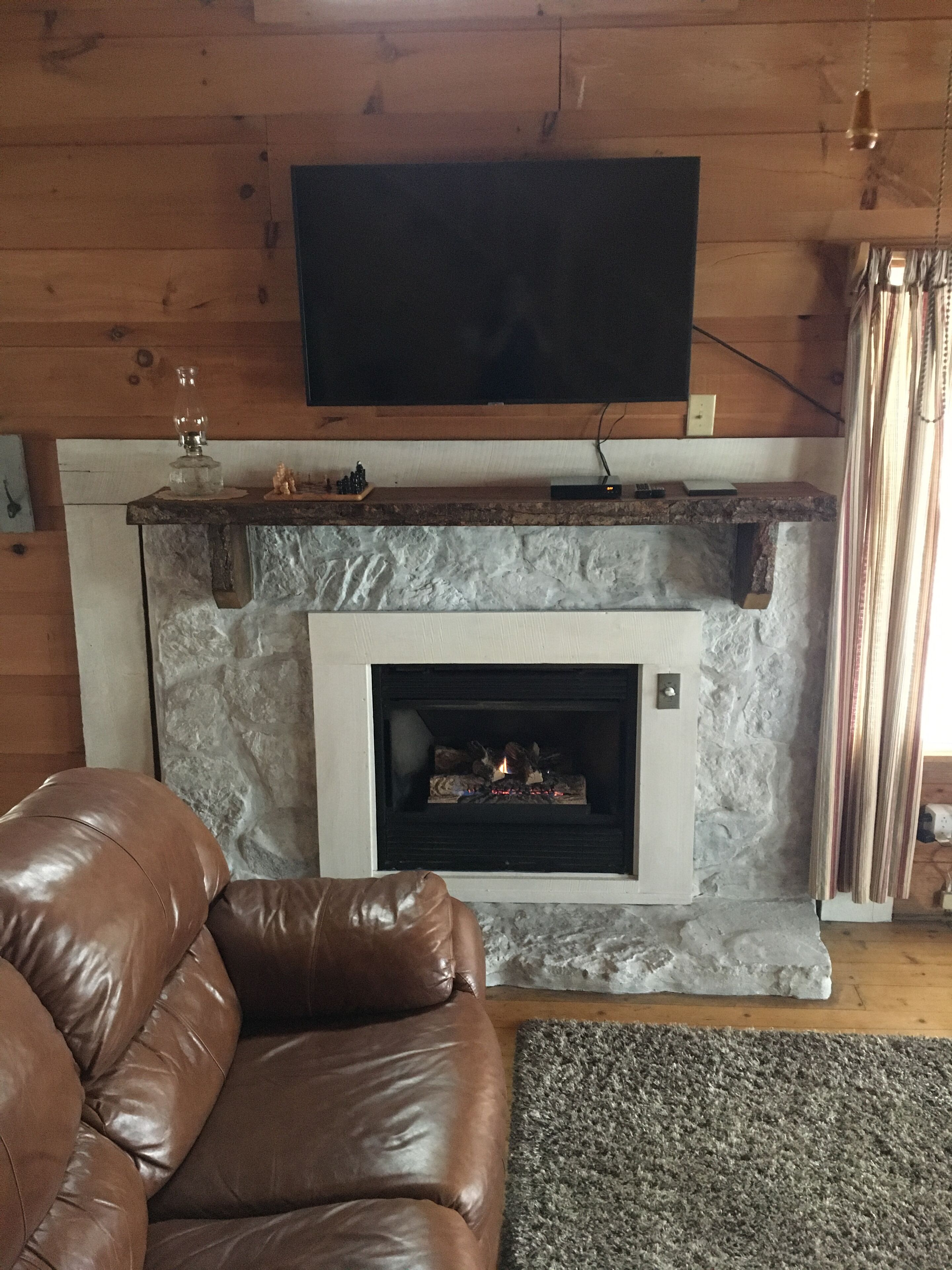 A living room with a stone fireplace, a leather sofa, and a flat-screen TV mounted above the fireplace.