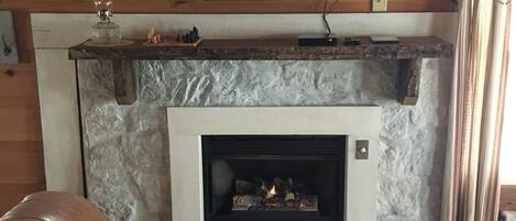 A living room with a stone fireplace, a leather sofa, and a flat-screen TV mounted above the fireplace.