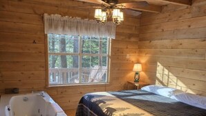 Un dormitorio de cabaña de madera con cama, ventana, ventilador de techo y bañera.