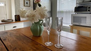A wooden table with a green vase and two clear wine glasses, a white microwave, and a window with blinds. - Magical Little Home in Historic District • Parking  • Rustic Luxury  • Outdoor.. (Marblehead)
