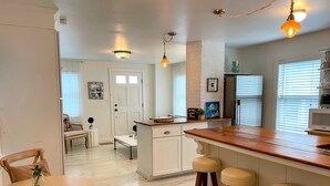 A kitchen with a wooden island, white cabinetry, and a dining area with a wooden table and chairs. - Magical Little Home in Historic District • Parking  • Rustic Luxury  • Outdoor.. (Marblehead)