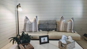 A cozy living room with a beige sofa, striped pillows, a small plant, a framed picture, and a basket with tissues. - Magical Little Home in Historic District • Parking  • Rustic Luxury  • Outdoor.. (Marblehead)