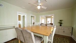 Une salle à manger avec une table et des chaises en bois, un ventilateur de plafond et un tapis à motifs.