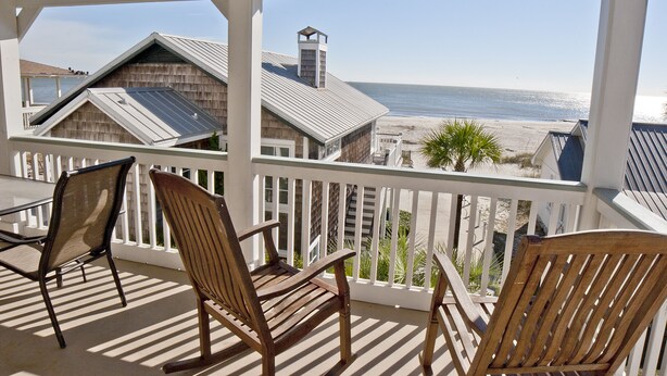 Un balcon avec des chaises en bois et vue sur la plage.