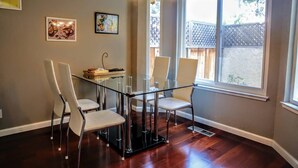 A dining area with a glass table and four chairs, a chandelier, and two framed pictures on the wall.
