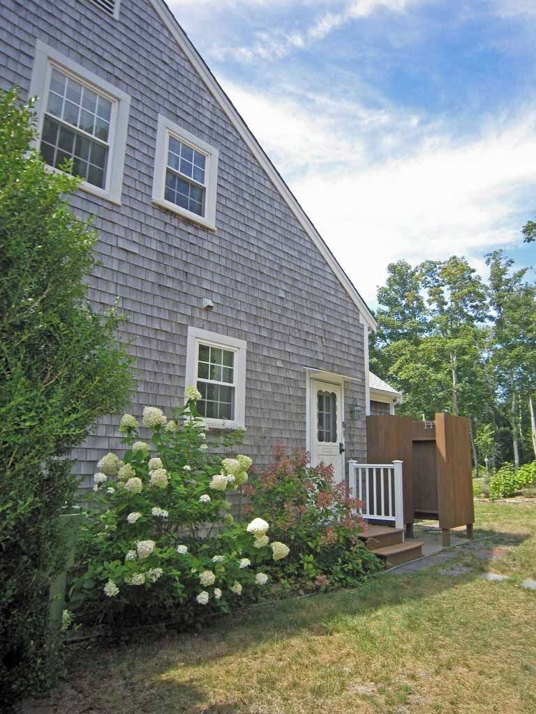 A two-story house with a gray shingled exterior, white trim, and a front porch with a wooden deck.