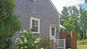A two-story house with a gray shingled exterior, white trim, and a front porch with a wooden deck.