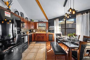 A modern kitchen with wooden cabinets, a stainless steel refrigerator, and a dining area with a bench and table set for two.