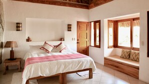 Un dormitorio con una cama grande, un banco de madera junto a la ventana y un techo de paja.
