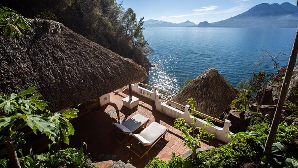 Un patio con sillones de descanso con vista a un cuerpo de agua y montañas.